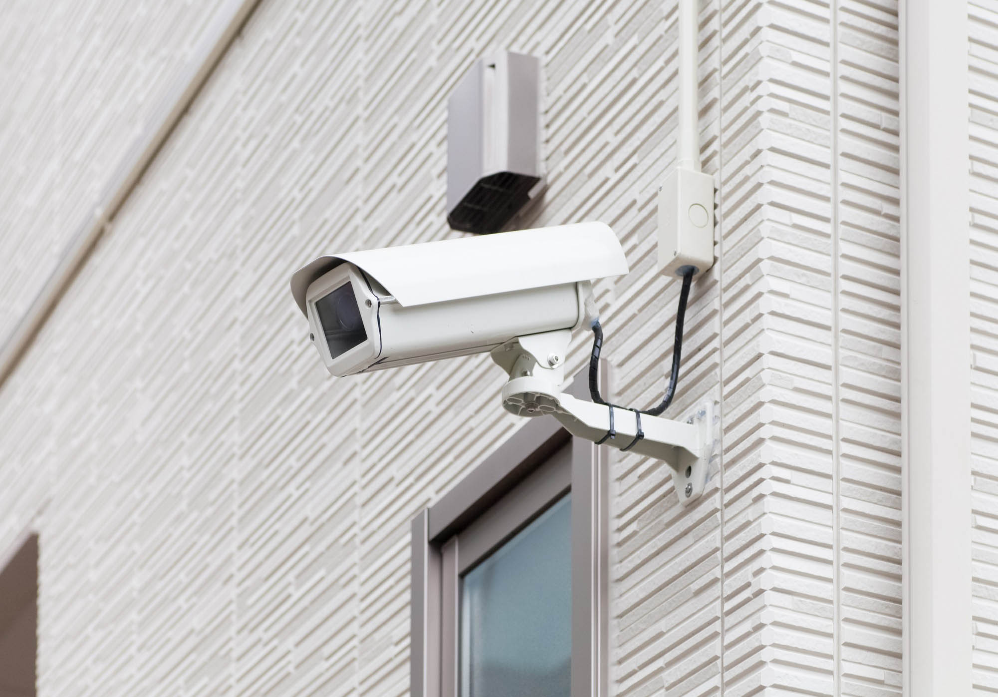 Surveillance camera mounted on a textured wall, designed for monitoring and security purposes. Ideal for discussions on safety technology.