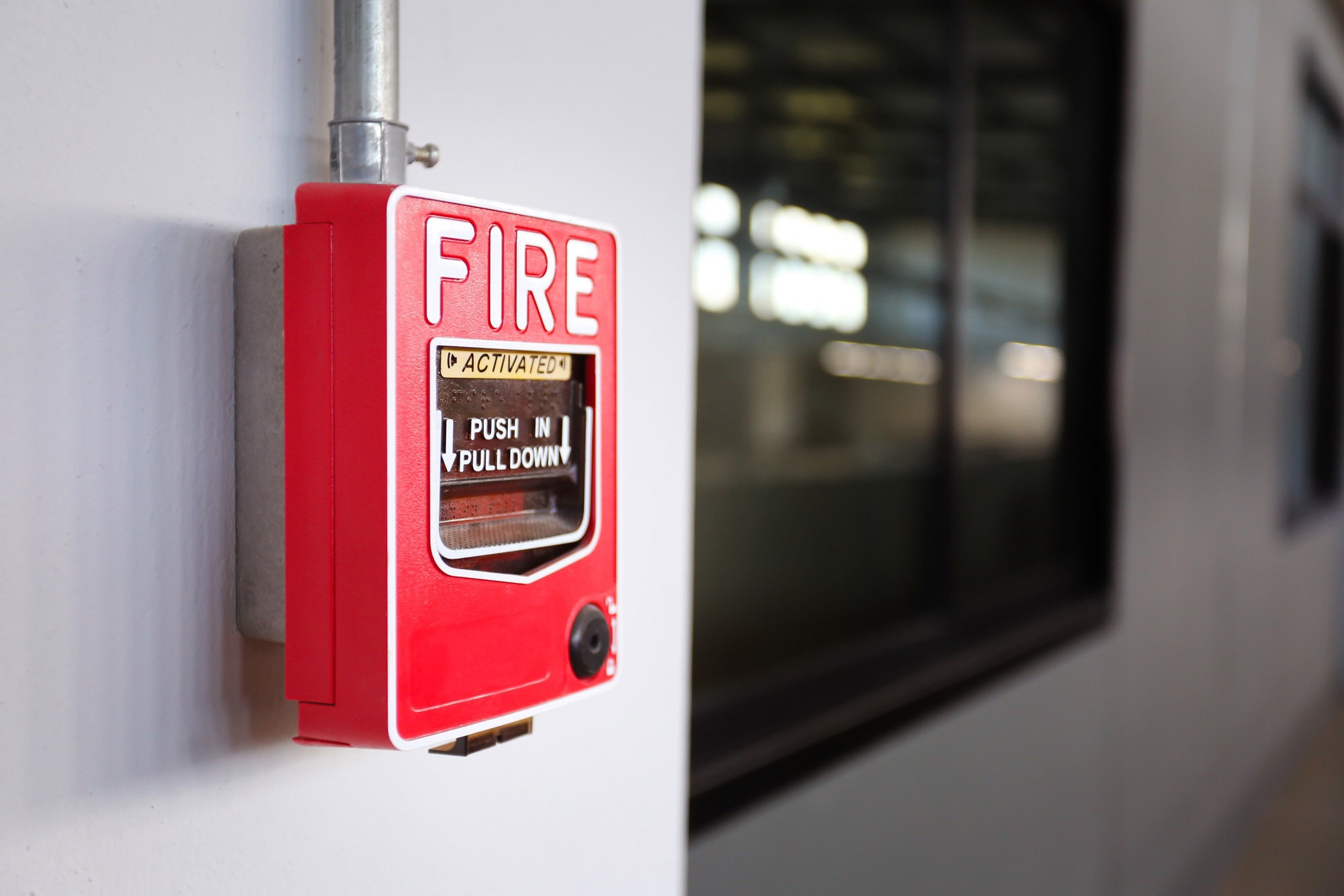 Red fire alarm pull station mounted on a wall, with instructions to "PUSH IN Pull Down." Relevant for safety protocols in the building.